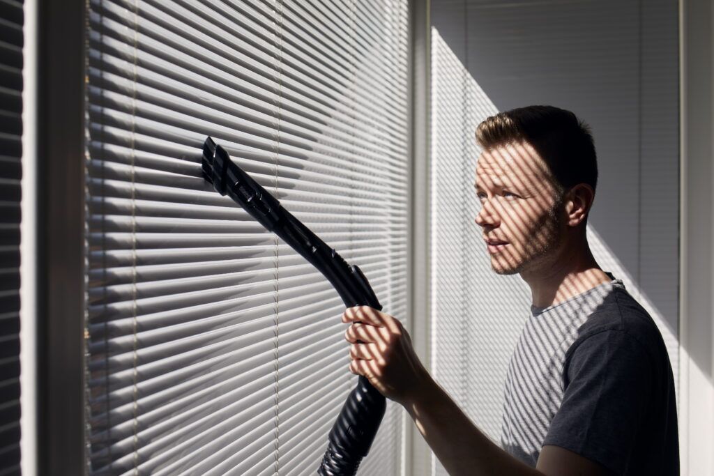 man vacuuming blinds